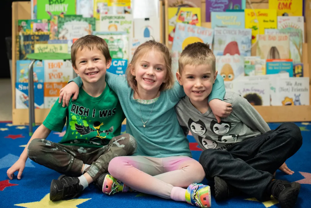 2 boys and 1 girl sitting on the floor smiling