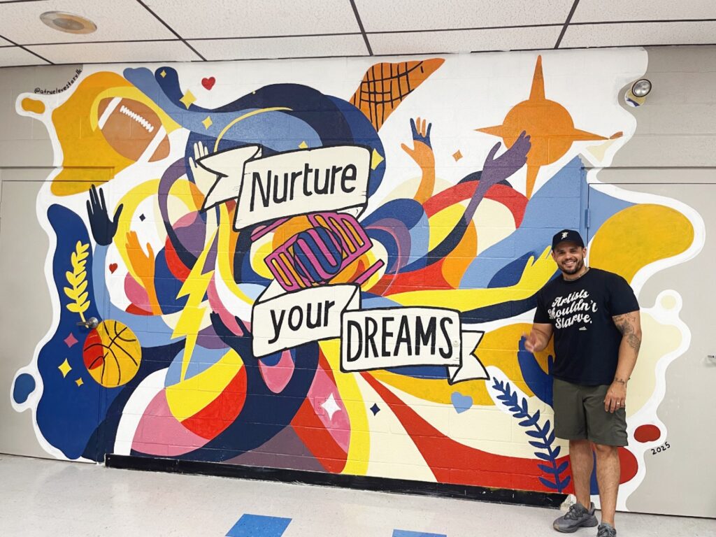 Muralist Kyle Edwards standing next to his mural at the Boys & Girls Club of Allentown